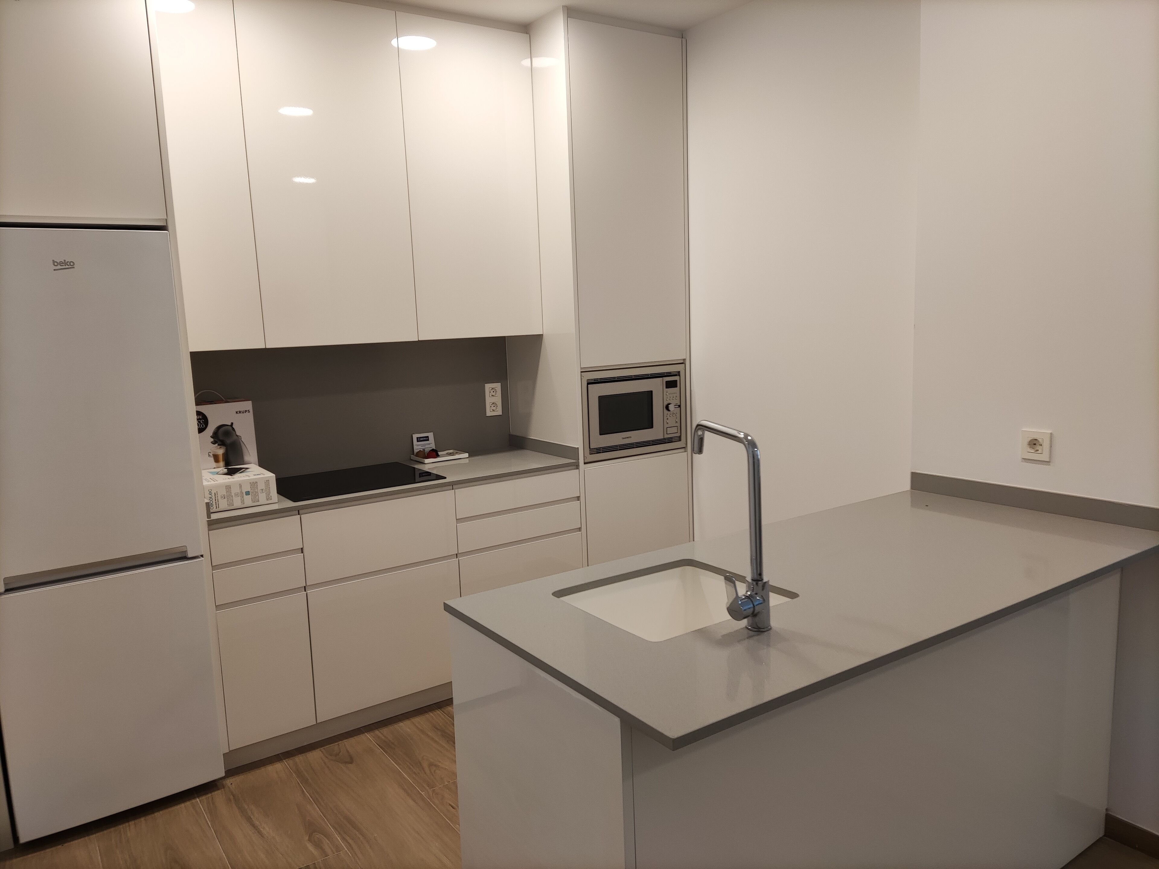Una cocina moderna con armarios blancos, microondas integrado y pileta de acero inoxidable.