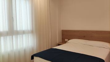 A bedroom with a bed, a wooden headboard, a nightstand, and sheer curtains.