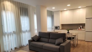 A modern living room with a grey sofa, a wooden coffee table, and a kitchen area with white cabinets and a microwave. - IBERFLAT APARTAMENTOS TRINIDAD (Castelló de la Plana)