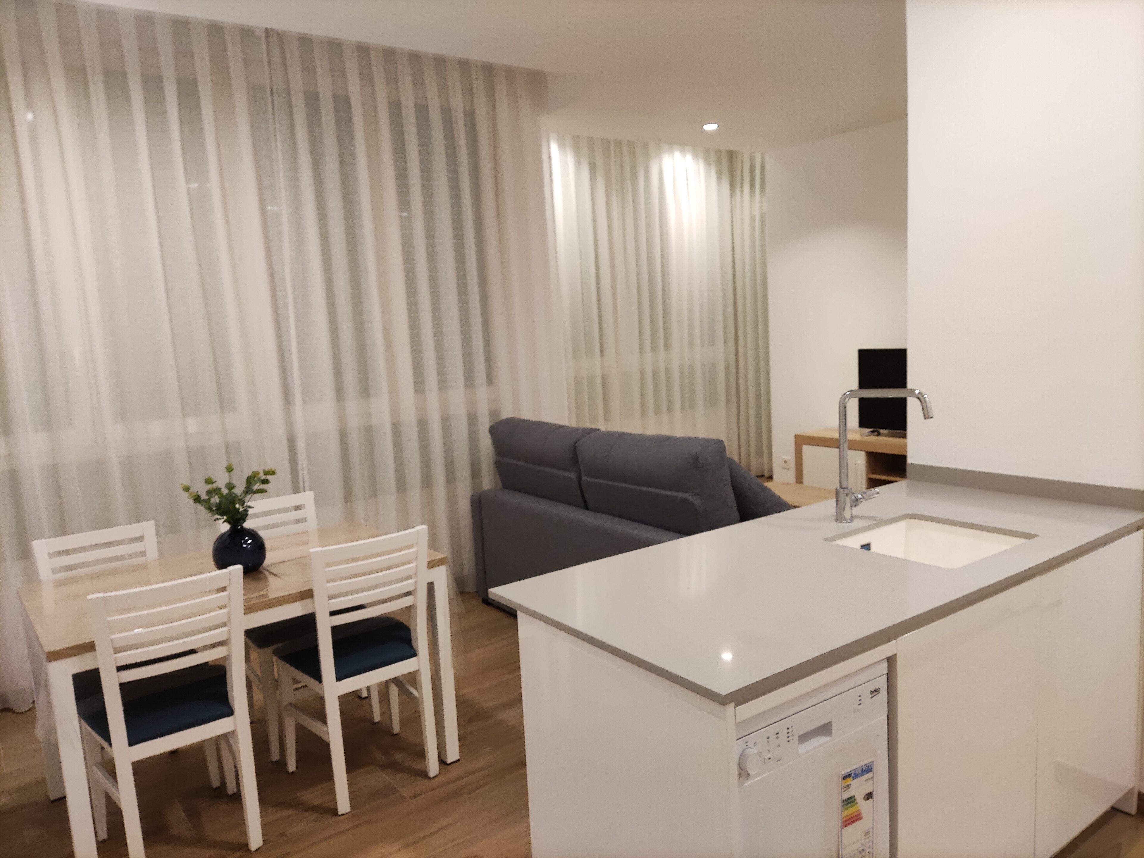 Een moderne keuken met een wit aanrecht, een ingebouwde vaatwasser en een grijze bank.