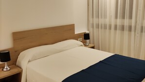 A neatly made bed with a wooden headboard, two bedside tables with lamps, and a window with sheer curtains. - IBERFLAT APARTAMENTOS TRINIDAD (Castelló de la Plana)