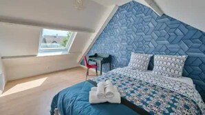 Un dormitorio con techo inclinado, cama con colcha estampada, dos almohadas y un juego de toallas sobre la cama.