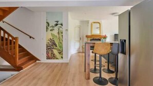 Un interior moderno con una escalera de madera, una zona de cocina con taburetes de bar y un mural en la pared.