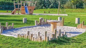Ein Spielplatz mit Rutsche und Klettergerüsten, umgeben von Sand und Rasenflächen.