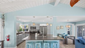 Cozinha moderna com ilha central, banquetas de bar e área de jantar com mesa e cadeiras.