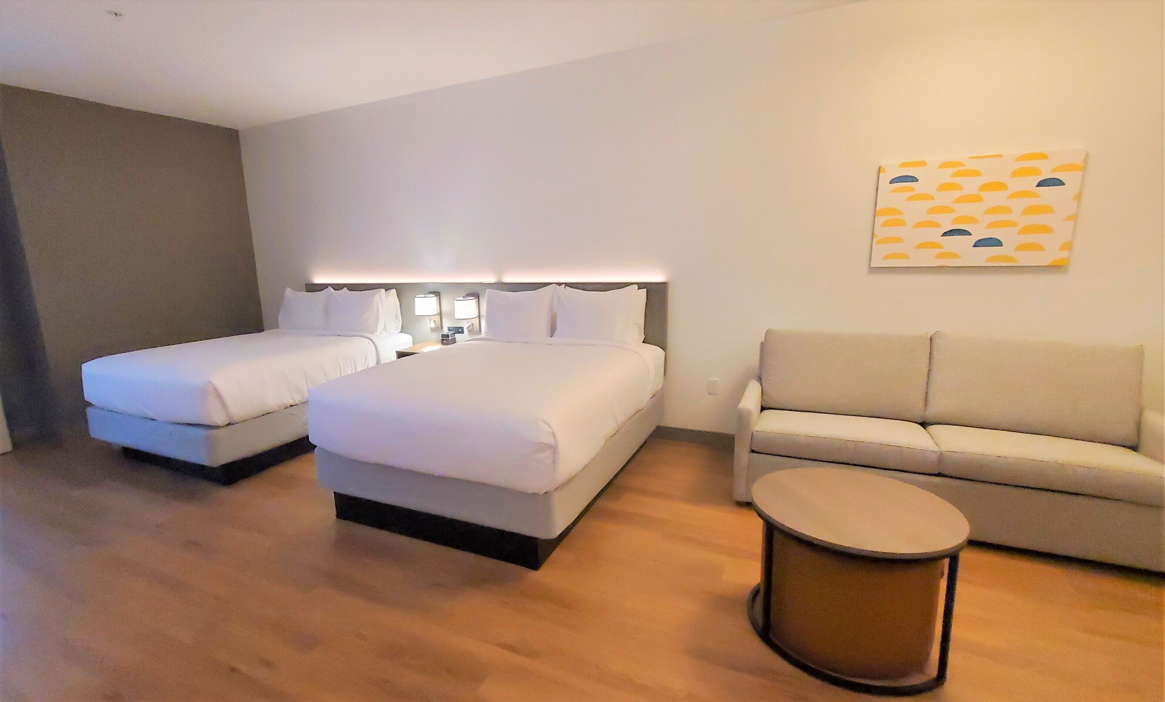 A hotel room with two beds, a sofa, a small round table, and a wall-mounted artwork.