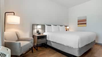 Quarto de hotel com cama, cadeira, mesa de cabeceira, abajur e um quadro na parede.