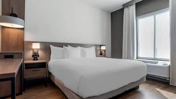 A modern hotel room with a large bed, bedside tables, a desk, and a window with curtains.