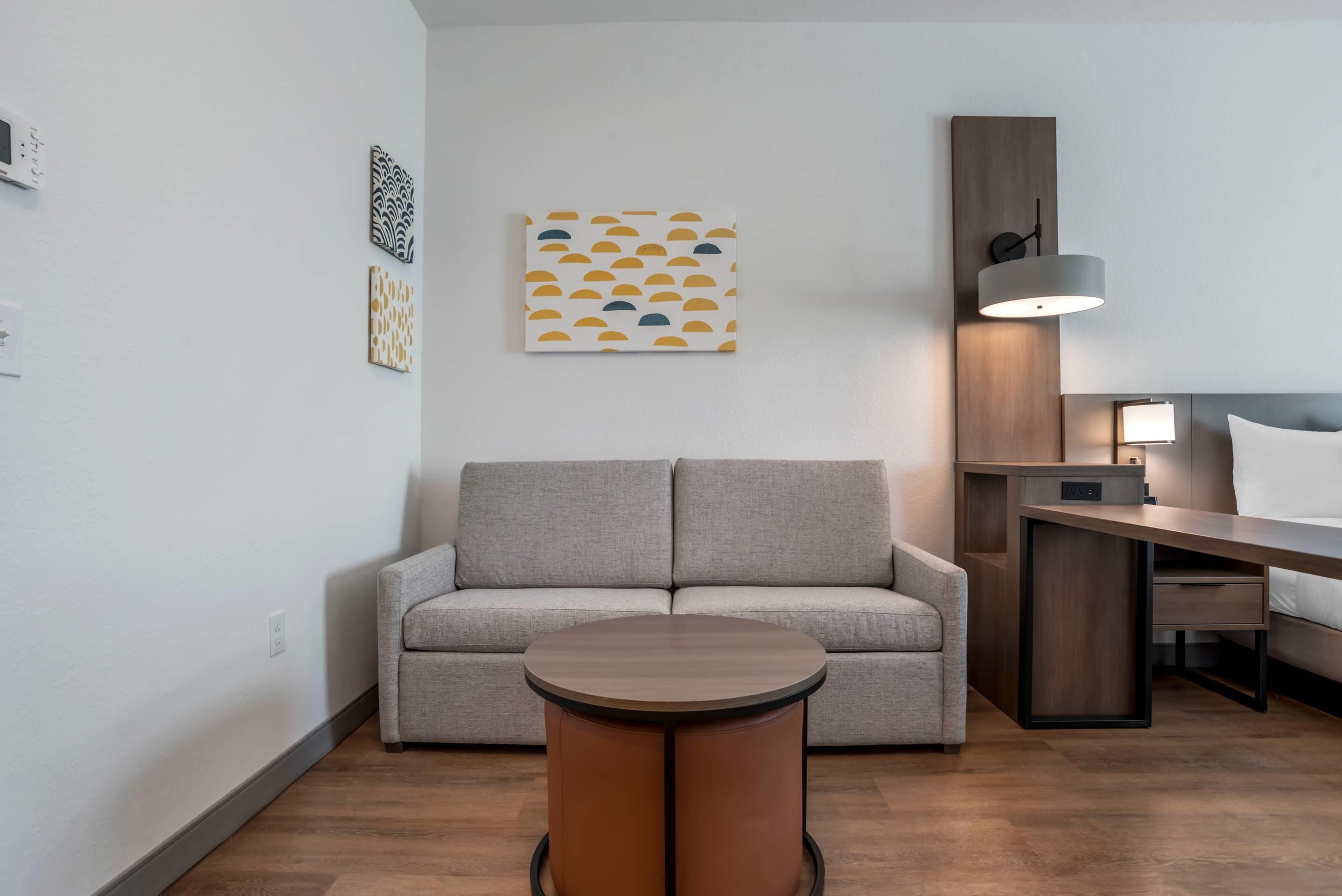 Una sala moderna con un sofá gris, una mesa de centro redonda y una mesita de noche de madera.