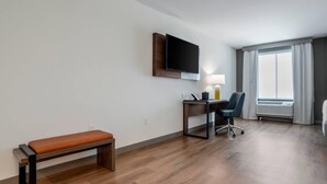 A hotel room with a wooden floor, a desk with a chair, a bench, a flat-screen TV mounted on the wall, and a window with curtains. - Comfort Inn & Suites Panama City Beach - Pier Park Area (Panama City Beach)