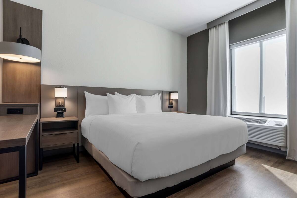 Une chambre d’hôtel moderne avec un grand lit, des lampes de chevet, un bureau et une fenêtre avec des rideaux.