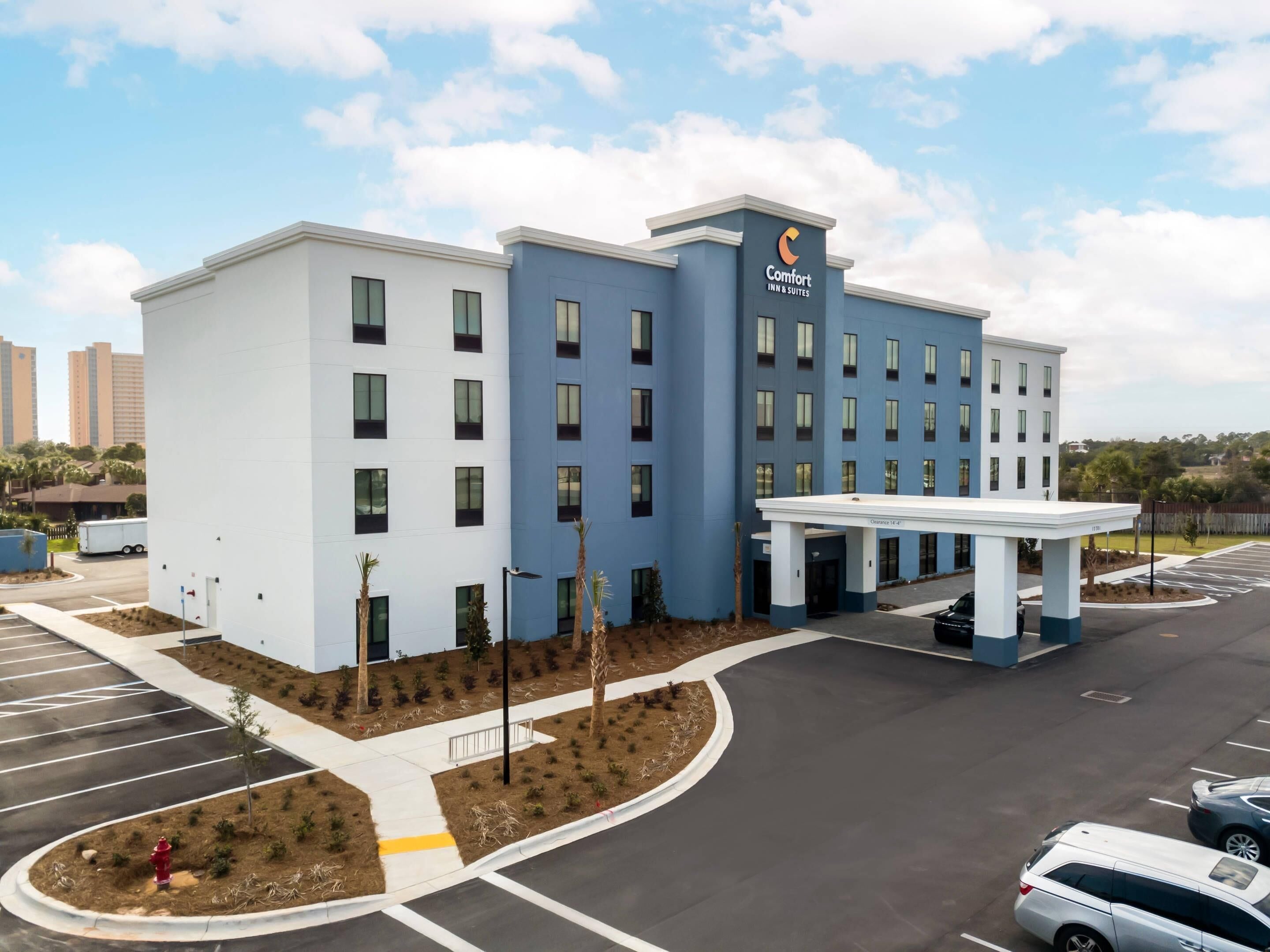 A hotel with a modern design, featuring a blue and white color scheme, a covered entrance, and a parking lot.
