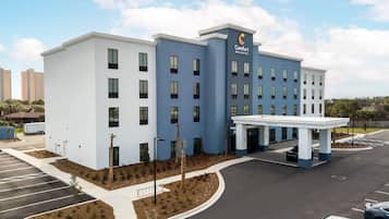 A hotel with a modern design, featuring a blue and white color scheme, a covered entrance, and a parking lot.