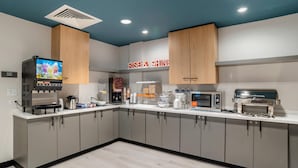 A modern kitchen with a coffee machine, microwave, and a digital screen displaying a fruit juice advertisement. - Comfort Inn & Suites Panama City Beach - Pier Park Area (Panama City Beach)