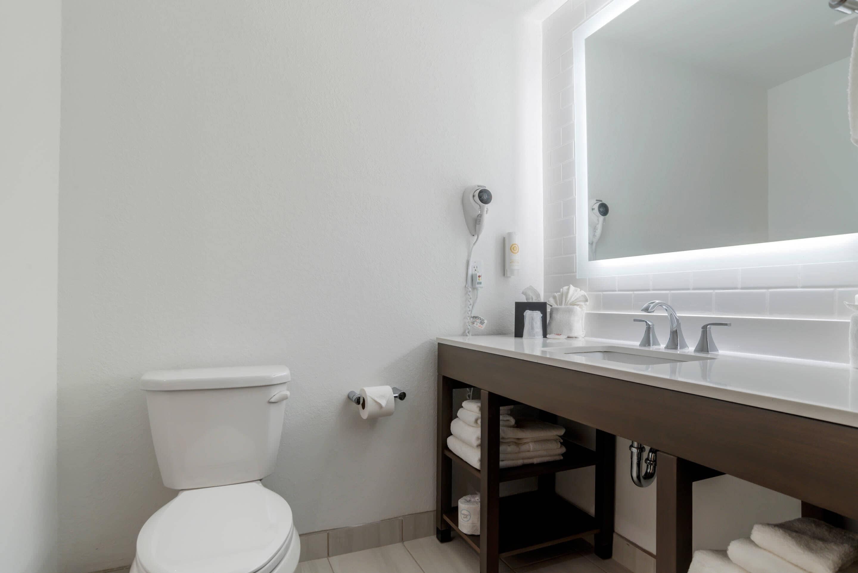 A modern bathroom with a white toilet, a large mirror above the sink, and a towel rack with folded towels.