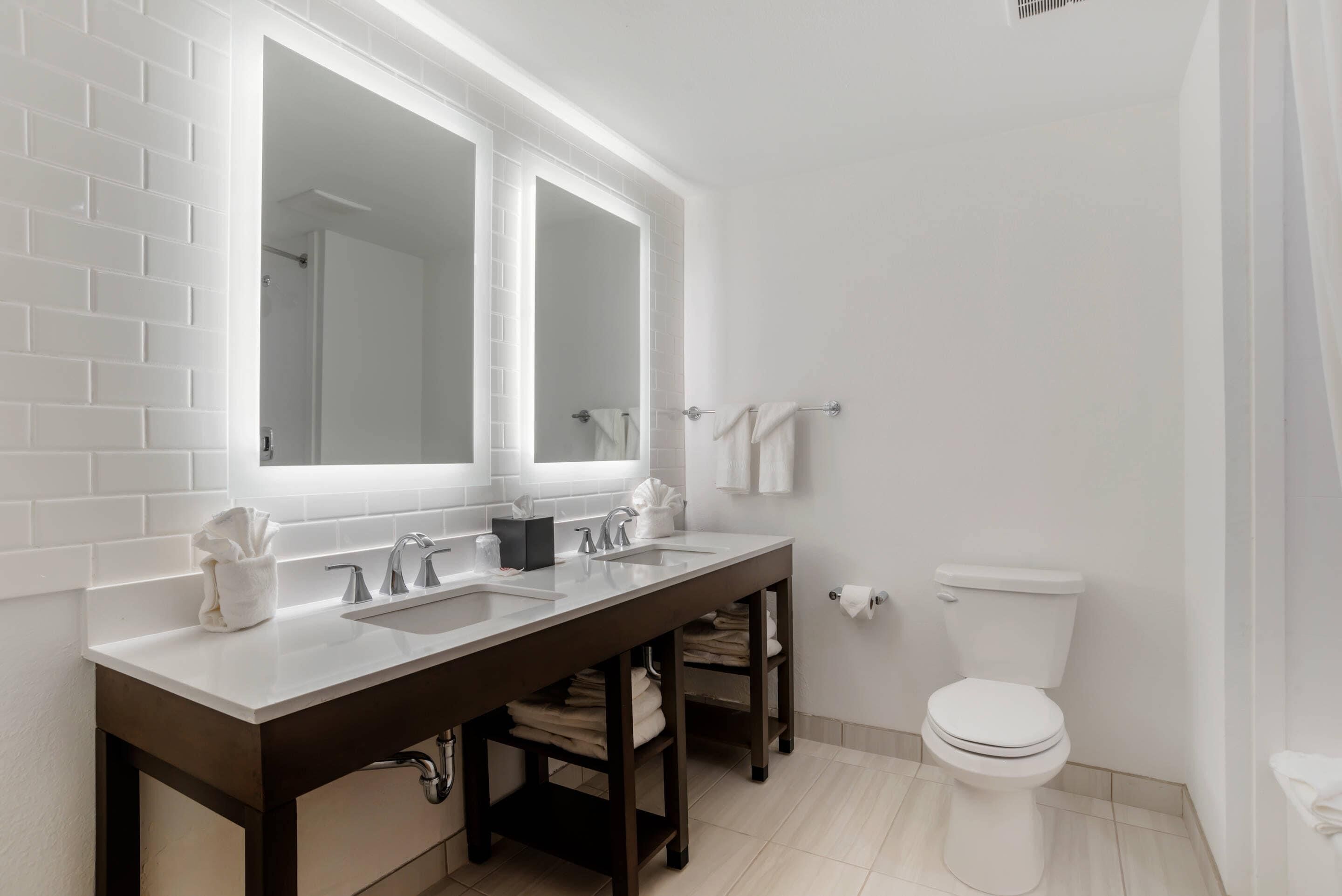 Un baño con lavamanos doble, inodoro y perchero para toallas.