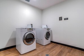Un lavadero con dos secadoras industriales LG y un letrero en la pared que indica los tiempos de ciclo y la disponibilidad de productos de lavandería.