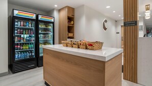 A reception area with a counter, a wall-mounted sign indicating a marketplace open 24 hours, and two refrigerated beverage dispensers. - Comfort Inn & Suites Panama City Beach - Pier Park Area (Panama City Beach)