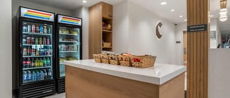 A reception area with a counter, a wall-mounted sign indicating a marketplace open 24 hours, and two refrigerated beverage dispensers.