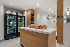 A reception area with a counter, a wall-mounted sign indicating a marketplace open 24 hours, and two refrigerated beverage dispensers. - Comfort Inn & Suites Panama City Beach - Pier Park Area (Panama City Beach)