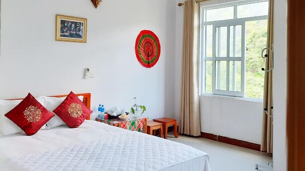 Une chambre d’hôtel comprenant un lit, une table de chevet, une lampe fixée au mur, un tableau encadré, une assiette décorative et une fenêtre avec des rideaux.