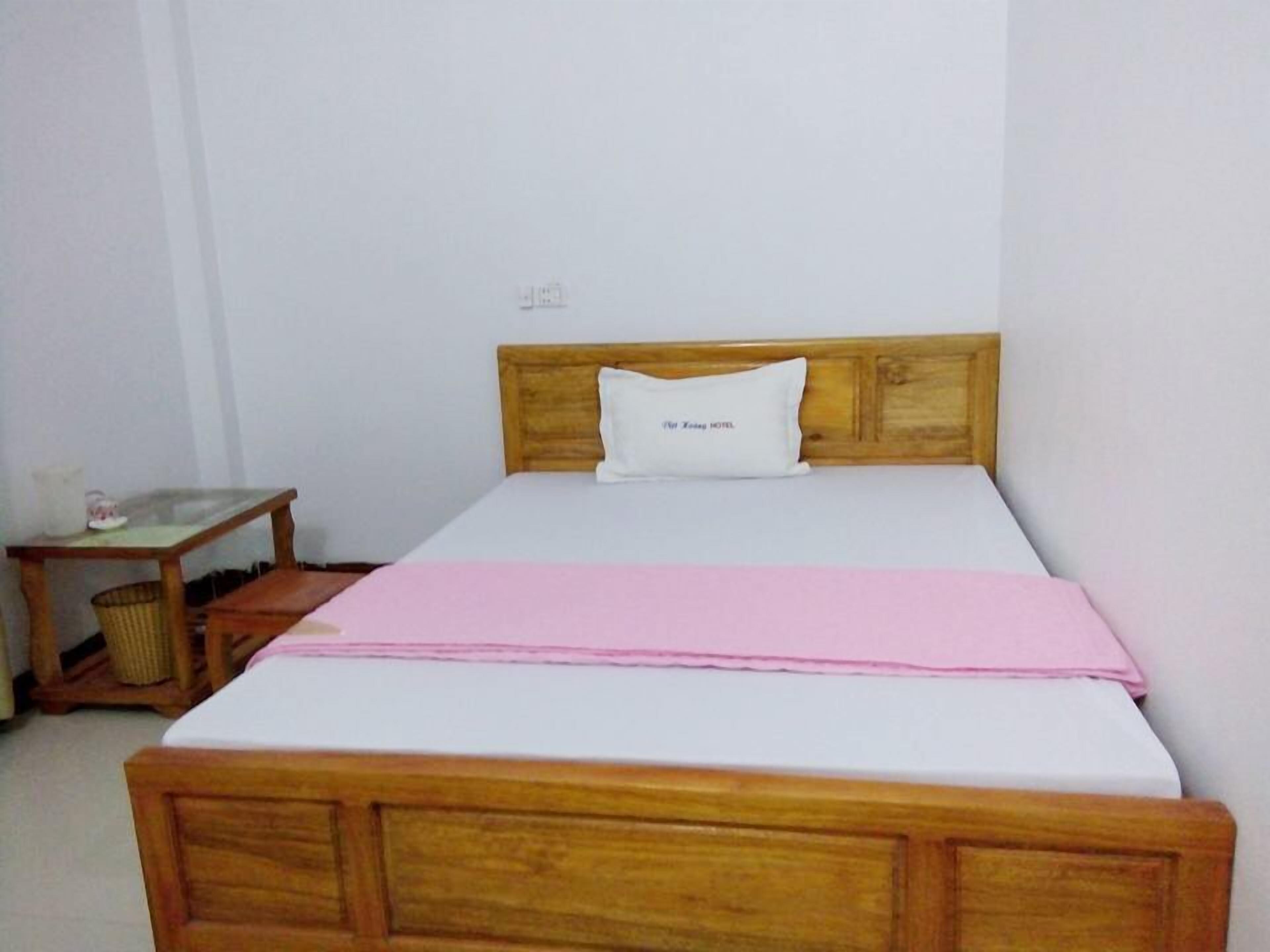A single-bed room with a wooden headboard, a bedside table with a lamp, and a pink bedspread.