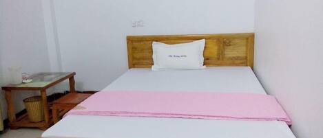 A single-bed room with a wooden headboard, a bedside table with a lamp, and a pink bedspread.