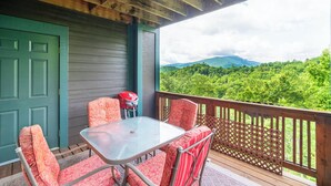 Un espace extérieur abrité, avec une table et des chaises, un barbecue rouge et une vue sur une chaîne de montagnes boisée.