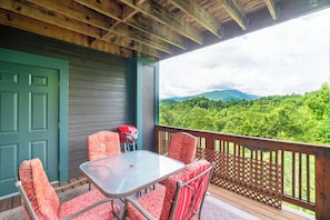 A covered outdoor seating area with a table and chairs, a red grill, and a view of a forested mountain range. - Evergreens 1522- Mtn Condo, Gated Resort, Indoor/Outdoor Pools & Hot Tub (Boone)