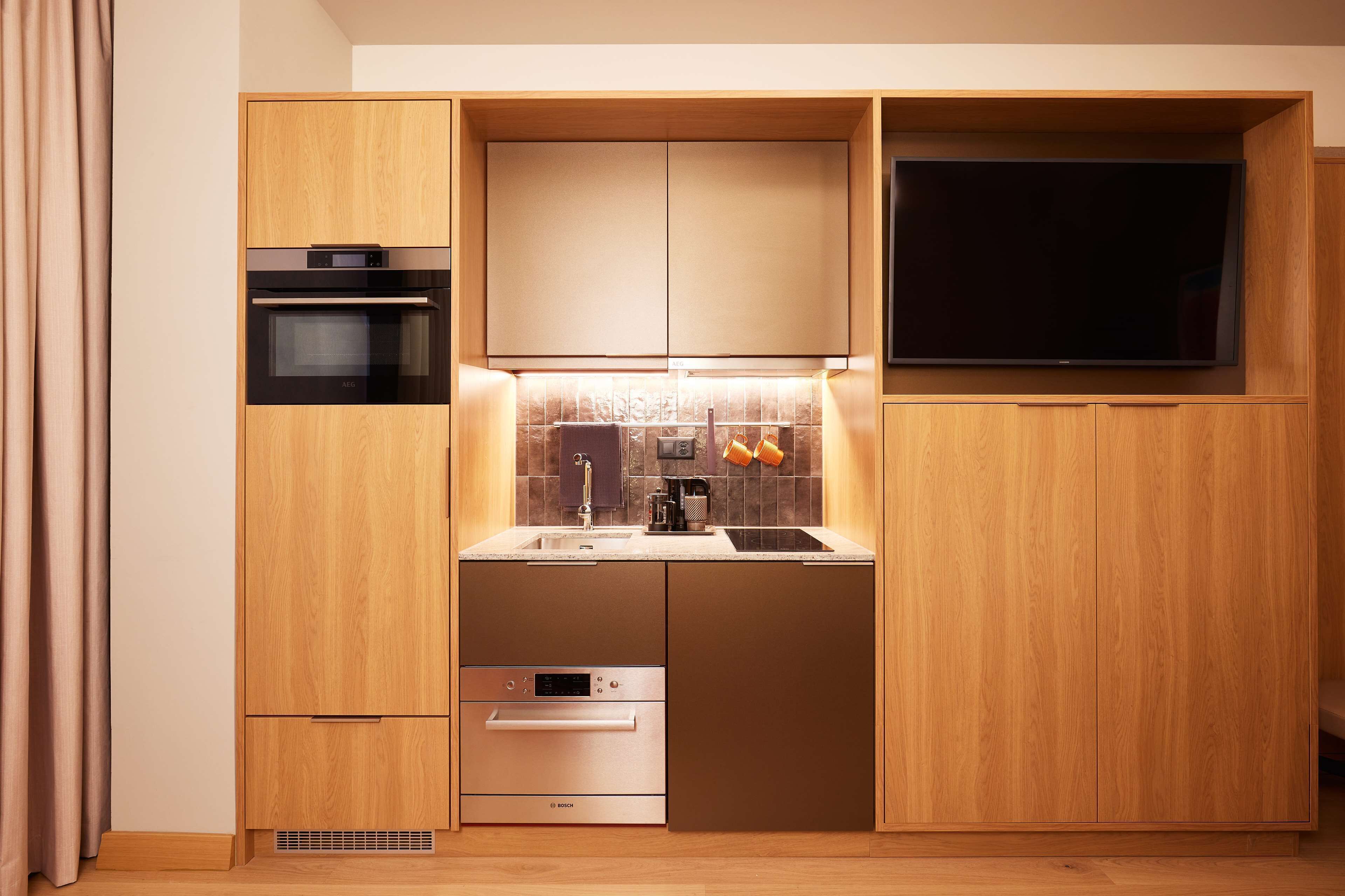 A compact kitchen with built-in appliances, a flat-screen TV, and a small countertop.