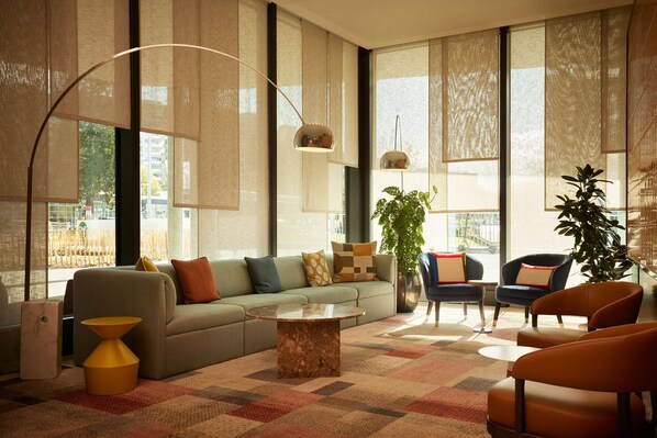 A modern living room with a sofa, armchairs, a coffee table, and large windows with sheer curtains. - Adina Apartment Hotel Geneva (Vernier)