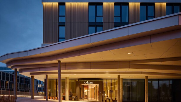 Een moderne hotelentree met een overdekte doorgang, grote ramen en een opvallend 'Adina' logo.