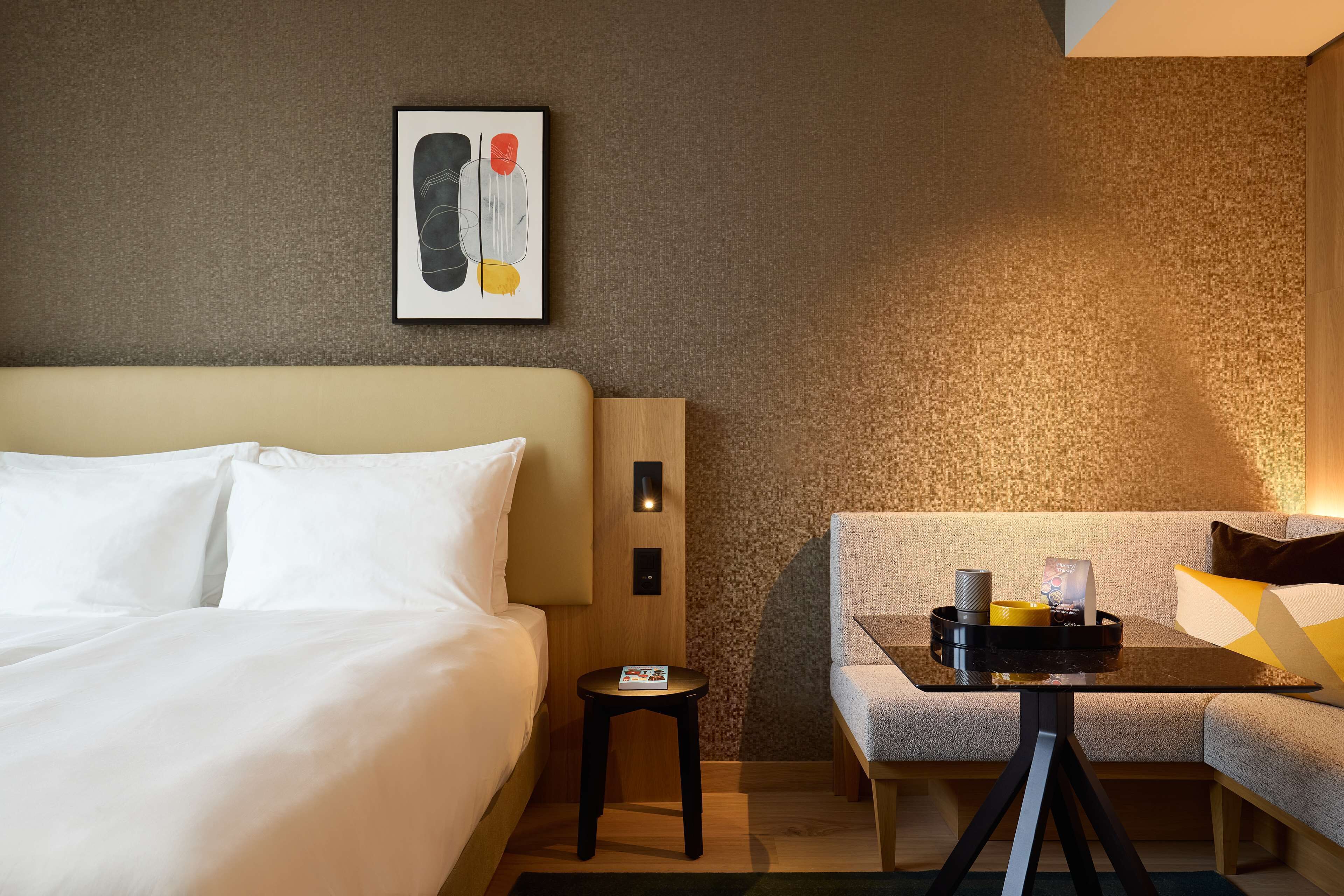 Habitación de hotel con cama, una mesita con bandeja, sofá y una lámpara de pared.