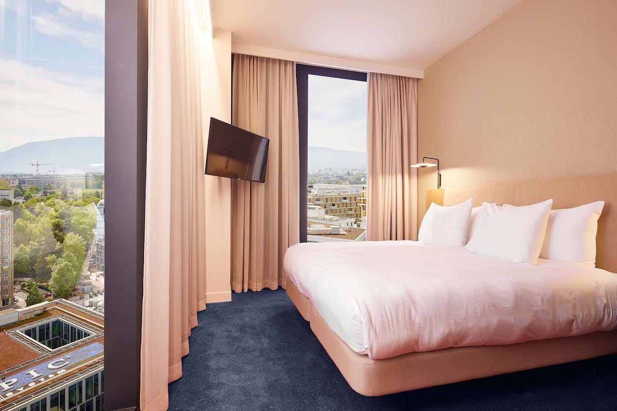 Habitación de hotel con una cama grande, un televisor montado en la pared y vistas a la ciudad.