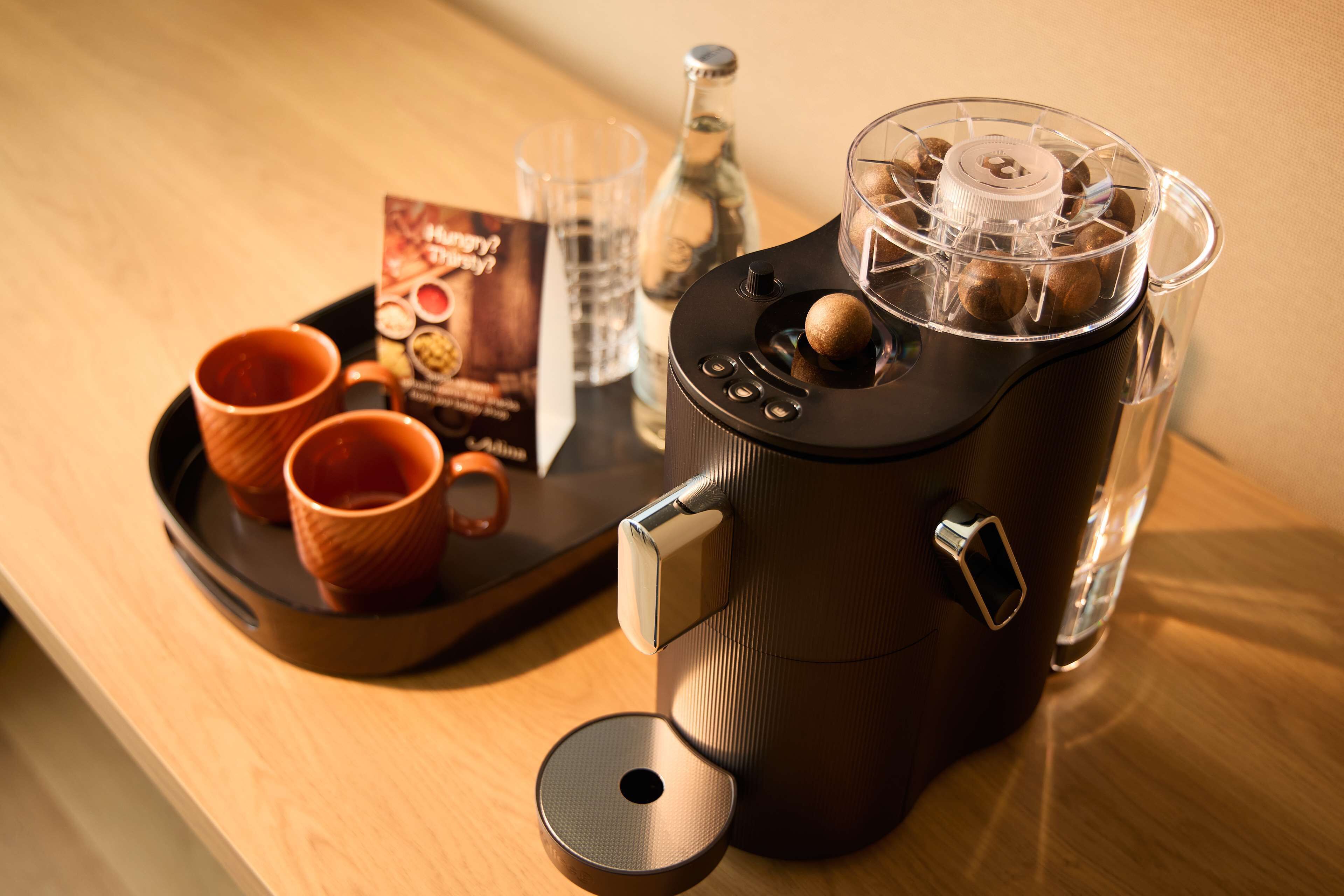 A coffee machine with a tray of two cups and a bottle of water.