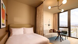 Een moderne hotelkamer met een groot bed, een bank, een kleintje tafeltje en uitzicht op de stad door grote ramen.