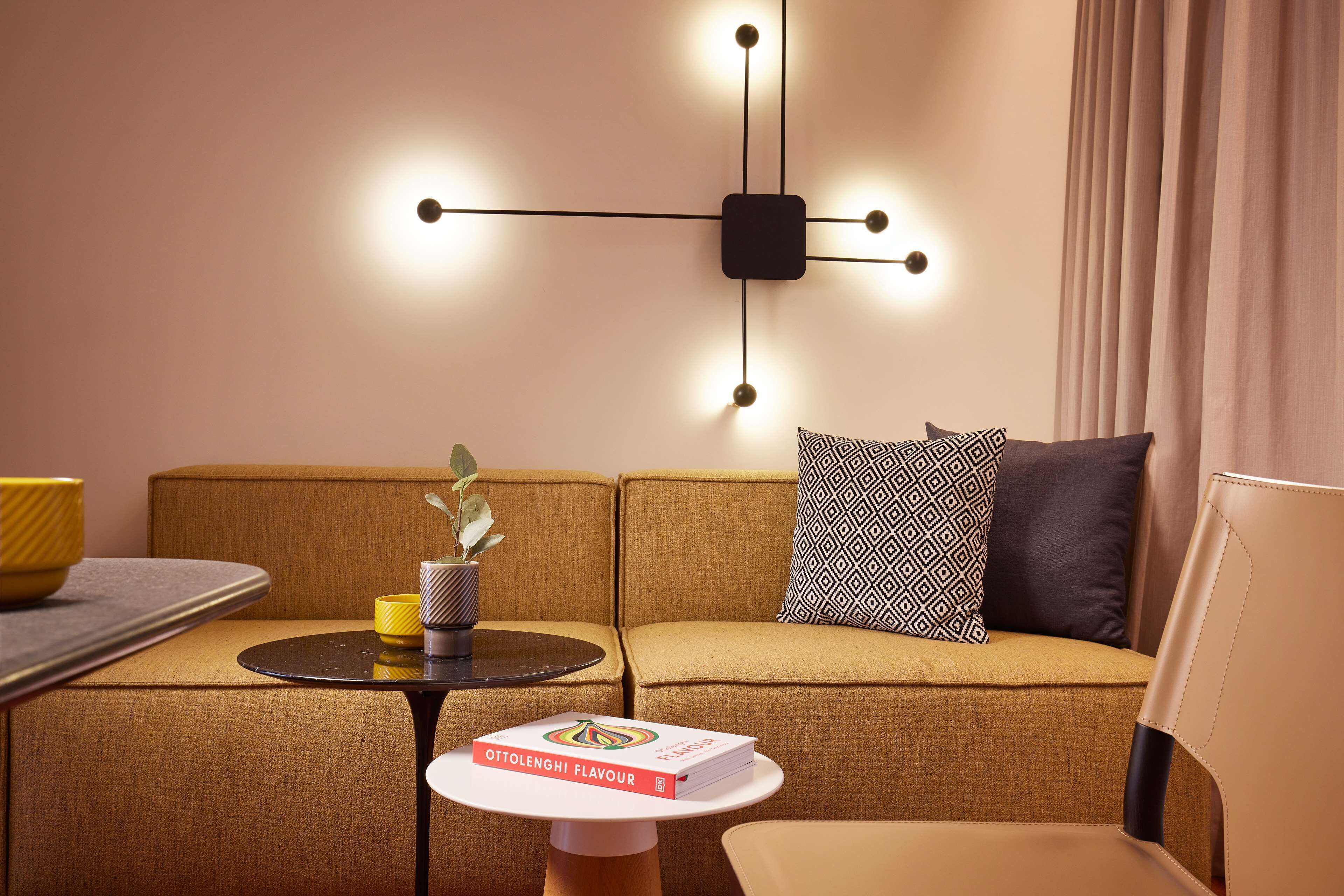 Een moderne woonkamer met een bank, een bijzettafeltje met een boek, een decoratieve wandlamp en een plant.