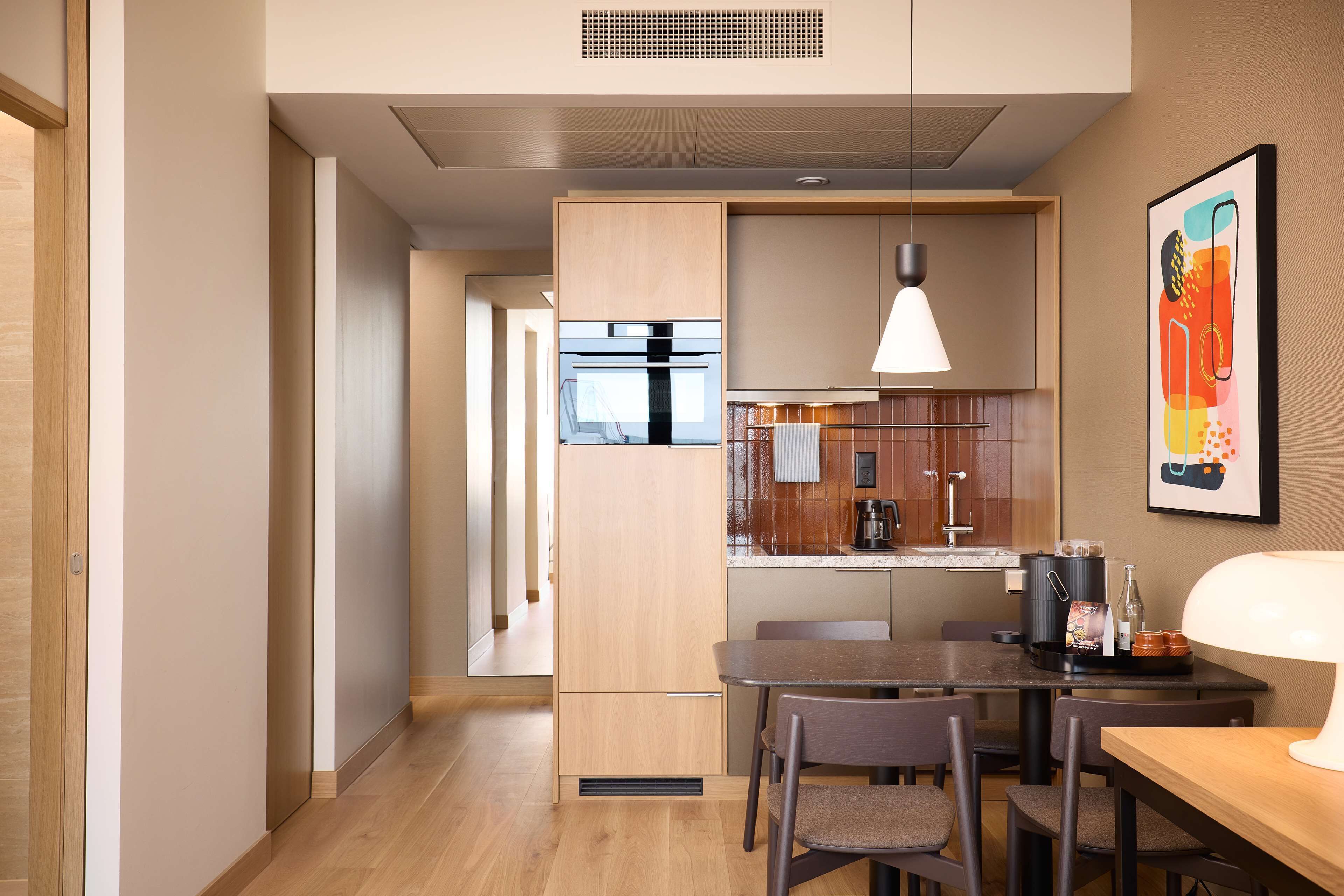 A modern kitchen with a dining area, wooden cabinets, a built-in oven, and a pendant light.