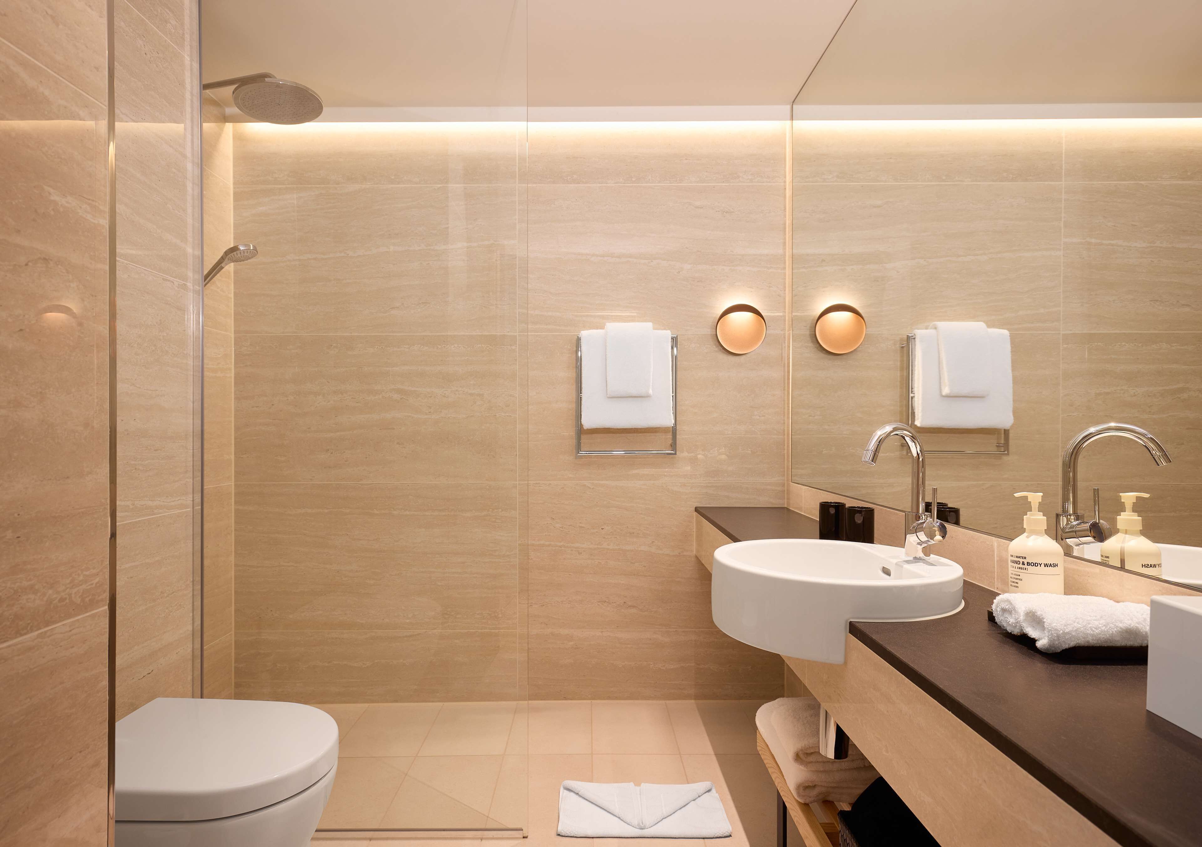 Une salle de bain moderne avec une douche à parois de verre, des toilettes blanches, un lavabo avec un miroir et deux porte-serviettes fixés au mur.