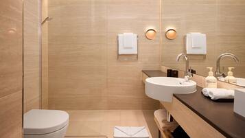 Une salle de bain moderne avec une douche à parois de verre, des toilettes blanches, un lavabo avec un miroir et deux porte-serviettes fixés au mur.