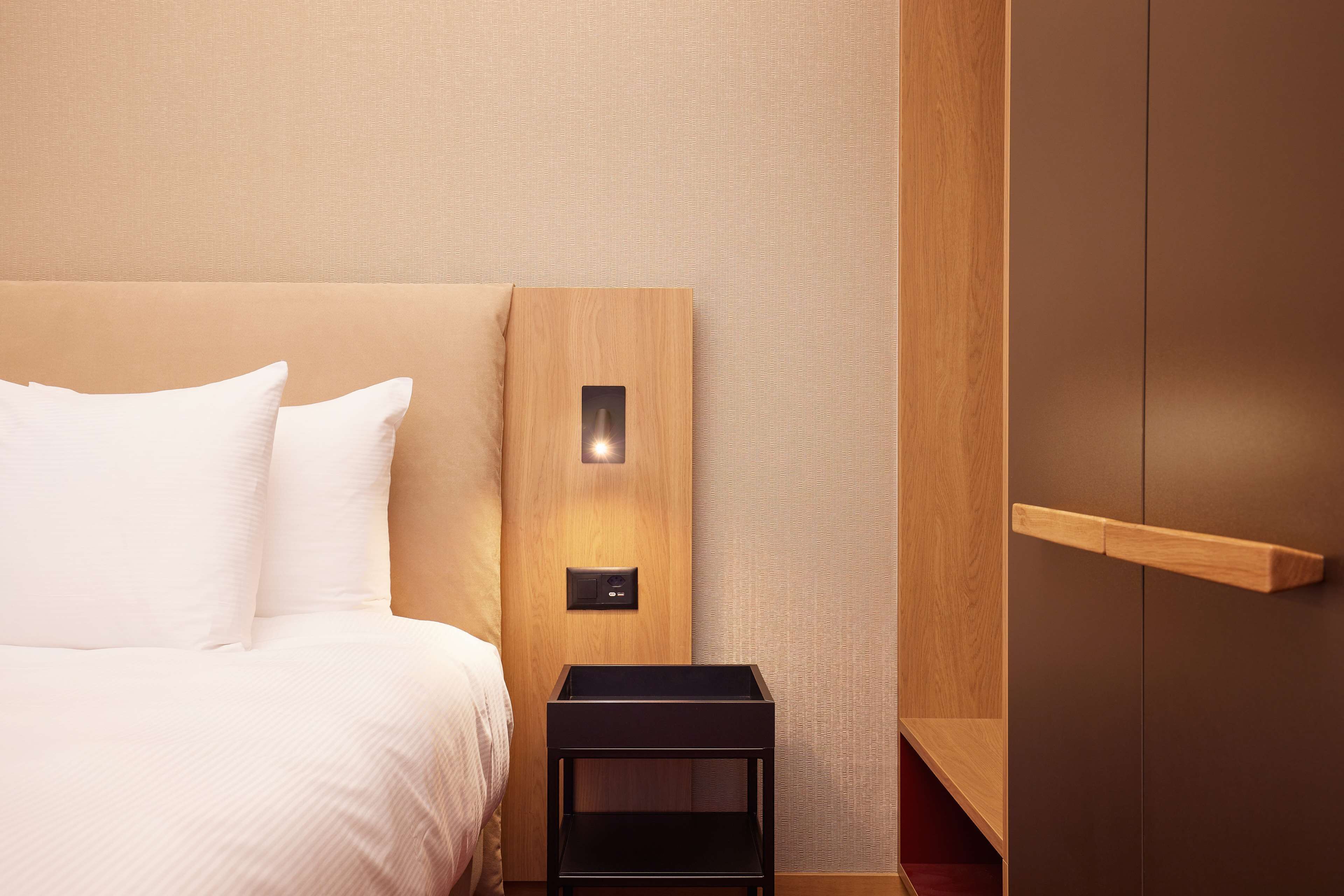 A hotel room with a bed, a nightstand, a wooden panel wall, and a wardrobe.