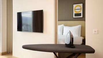 A hotel room with a flat-screen TV mounted on the wall, a bed with white bedding, and an ironing board with an iron.