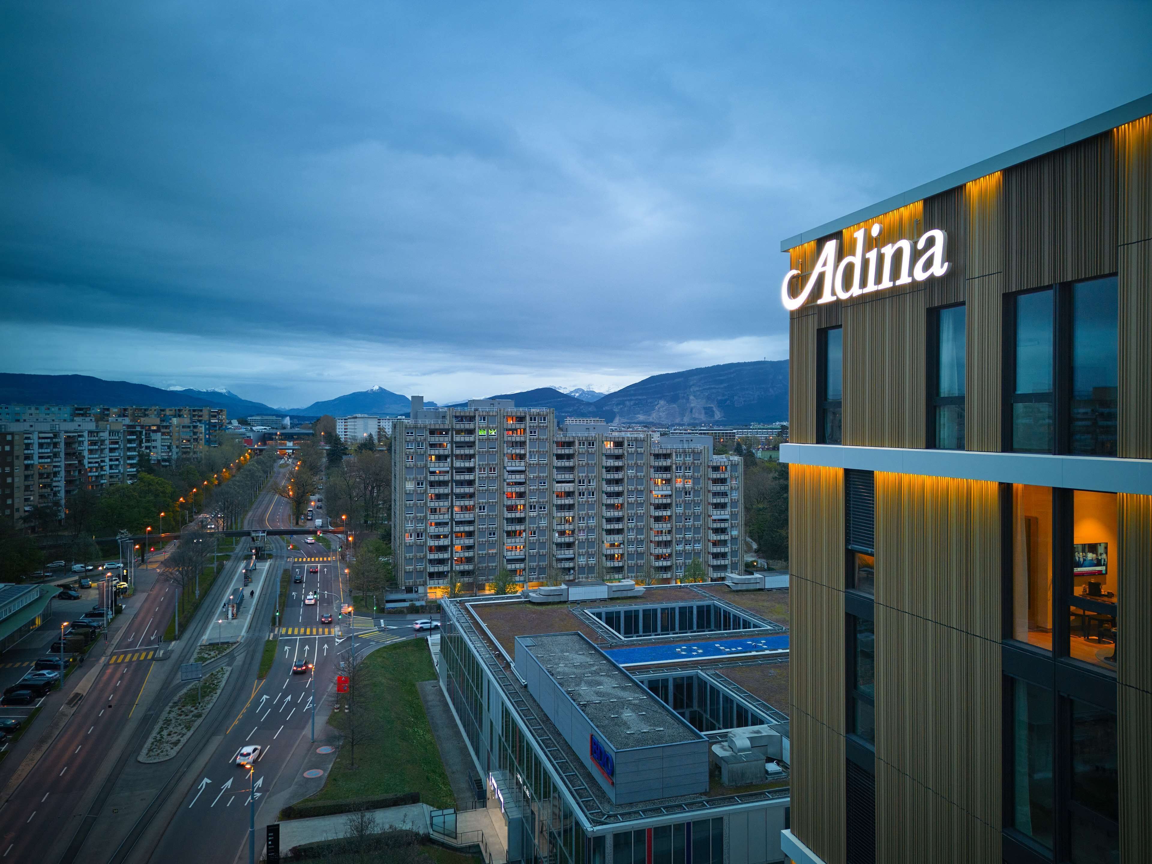 A modern building with the name 'Adina' illuminated on the facade.