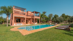 Una casa de dos pisos con piscina, mobiliario exterior y palmeras.