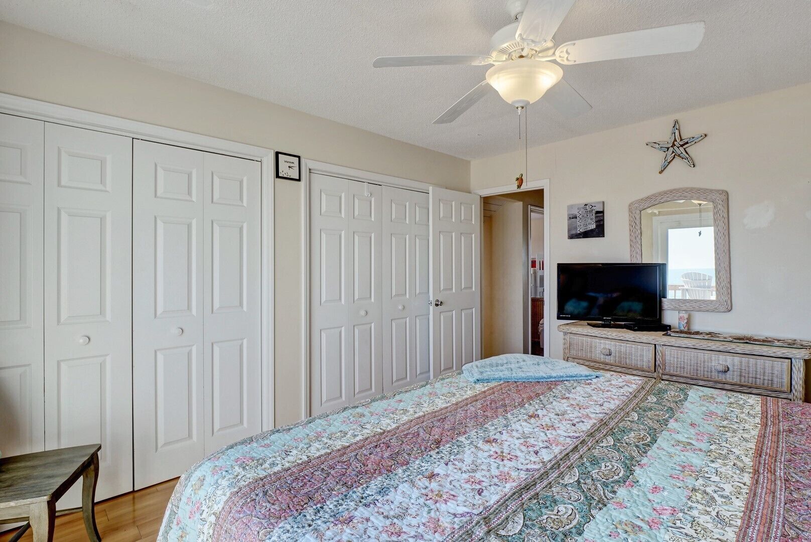 A bedroom with a bed, a television, a ceiling fan, and a wardrobe.