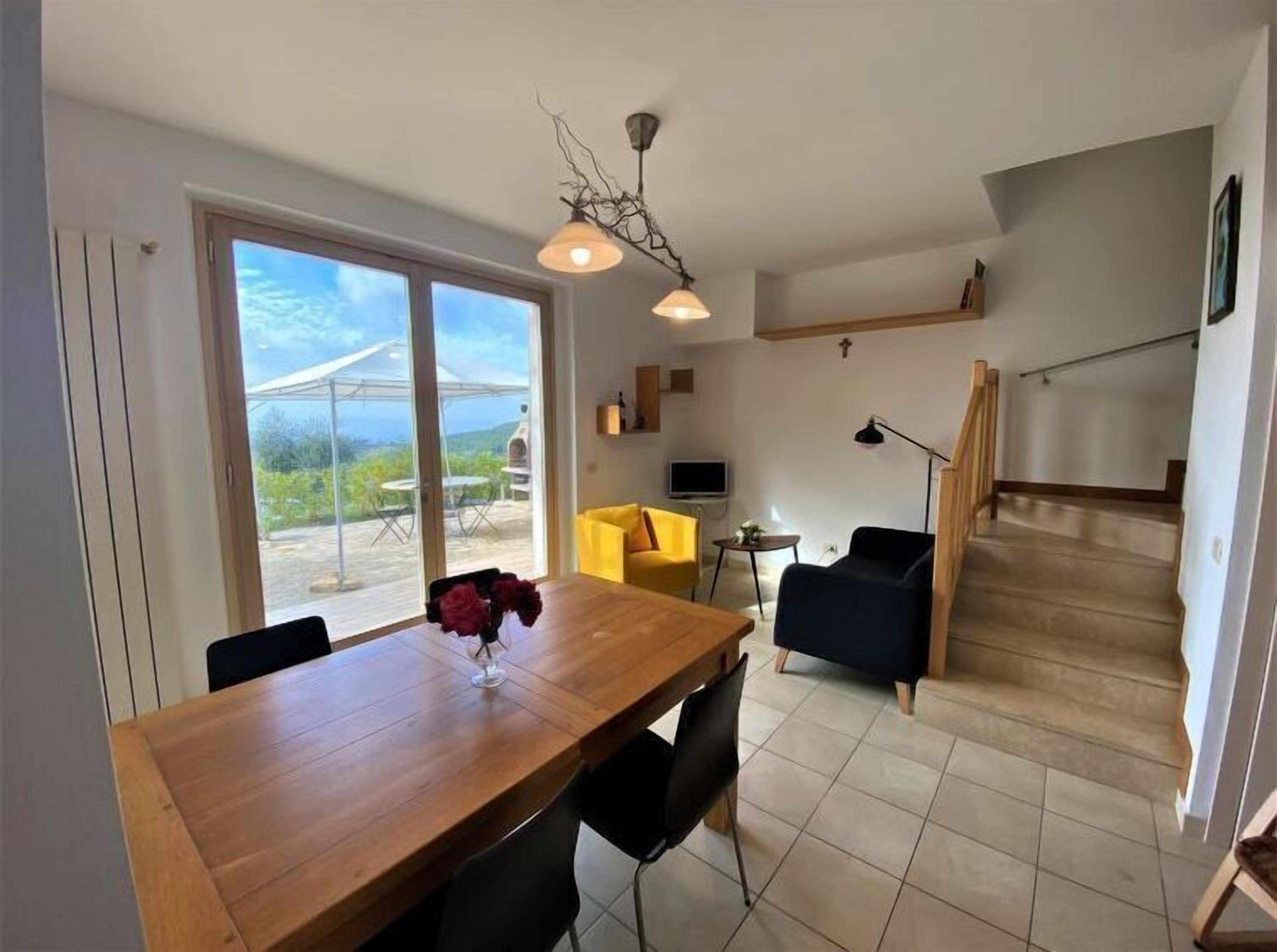 A modern living space with a wooden dining table, black chairs, a yellow sofa, and a staircase.