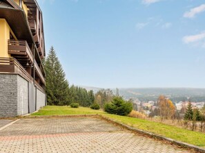 A building with a stone facade and wooden balconies overlooking a grassy area with trees and a distant view of a town.