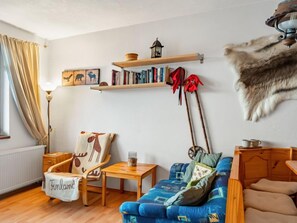 Una sala de estar acogedora con un sofá azul, una silla de madera, una mesita pequeña y una estantería.