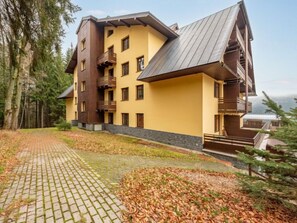 Un hotel de varios pisos con fachada amarilla, balcones de madera y un acceso pavimentado.