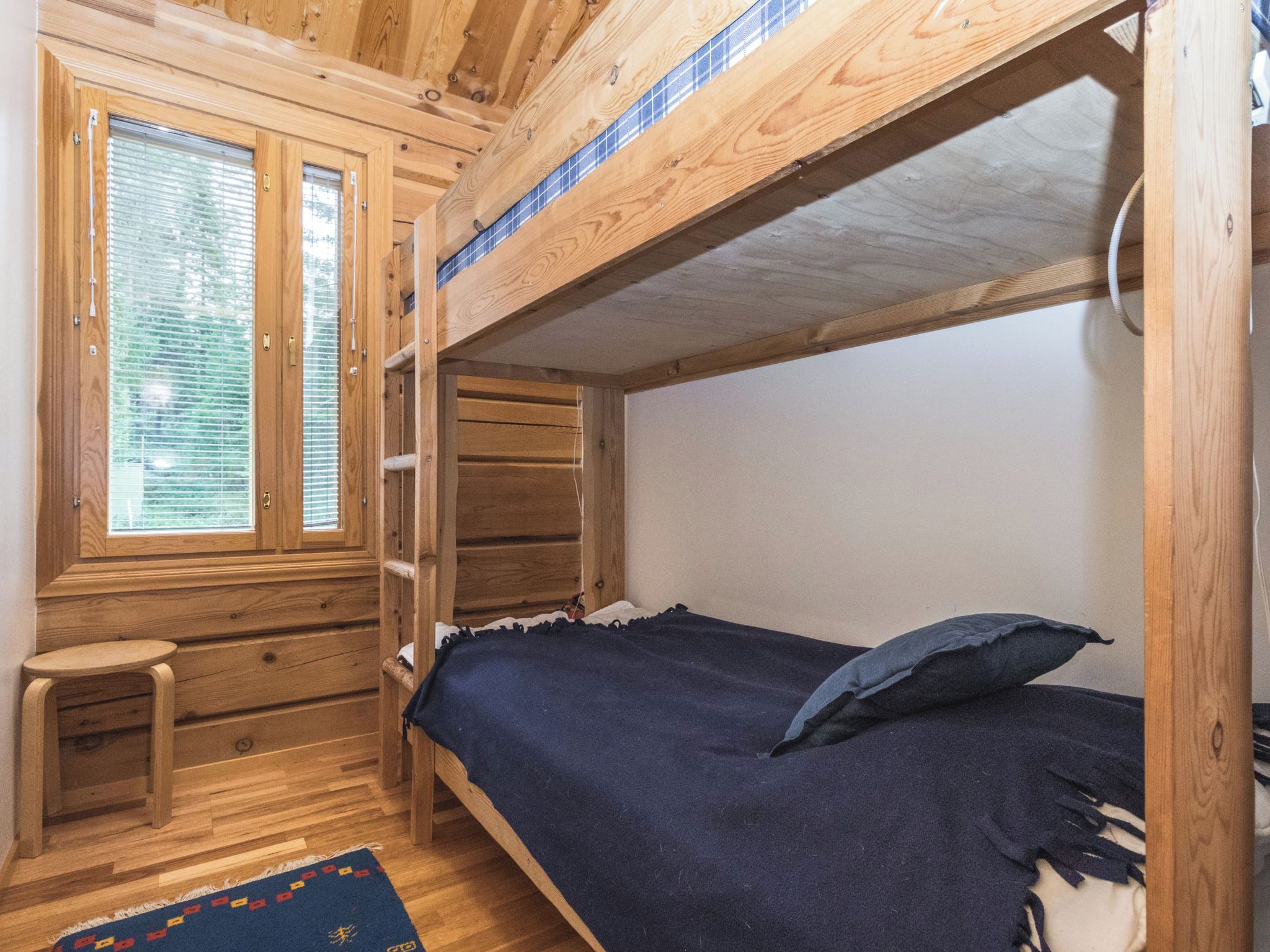 Dormitorio con literas, ventana, un taburete pequeño y una alfombra.